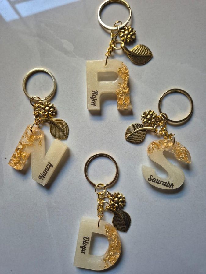 Four cream resin letter keychains with gold flakes, each engraved with a name